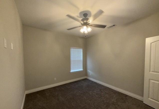 empty room featuring dark colored carpet, visible vents, baseboards, and a ceiling fan