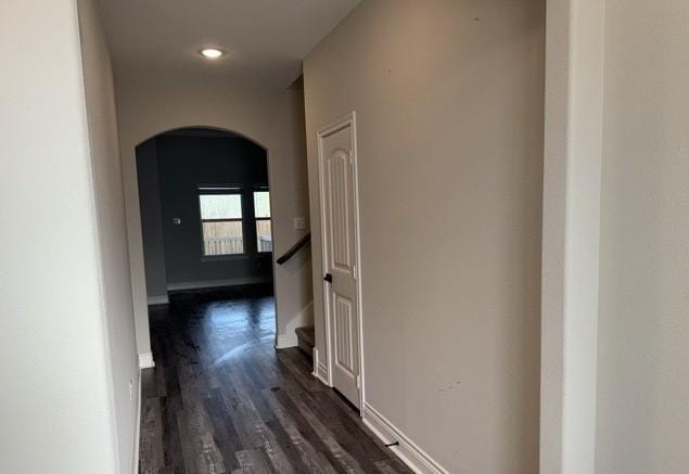 hall with arched walkways, baseboards, and dark wood finished floors