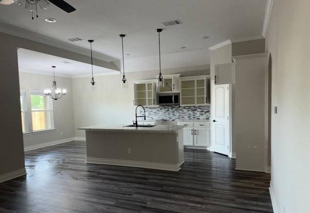 kitchen featuring stainless steel microwave, ornamental molding, decorative backsplash, ceiling fan with notable chandelier, and a sink