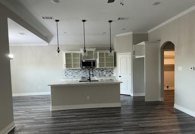 kitchen featuring stainless steel microwave, a ceiling fan, a kitchen island with sink, arched walkways, and a sink