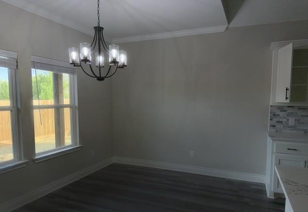 unfurnished dining area featuring ornamental molding, baseboards, an inviting chandelier, and dark wood finished floors