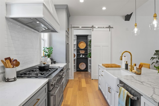 kitchen featuring a sink, a barn door, stainless steel appliances, light wood-type flooring, and custom exhaust hood