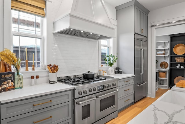 kitchen with gray cabinetry, premium range hood, light wood-type flooring, high end appliances, and backsplash