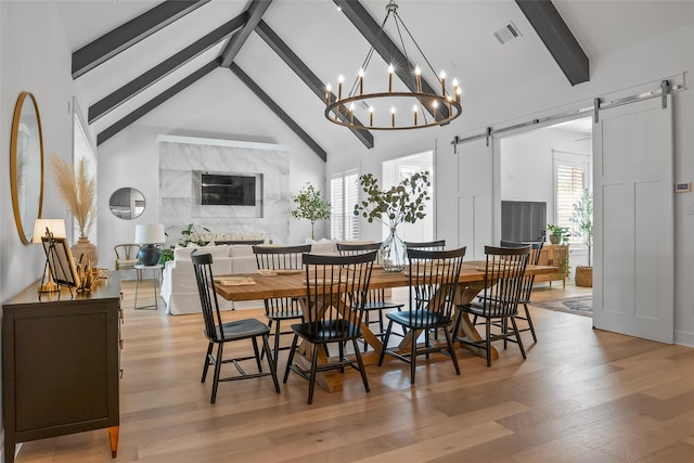 dining room with light wood finished floors, a barn door, visible vents, and beamed ceiling