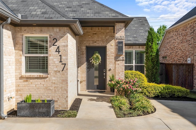 view of exterior entry with fence and a shingled roof