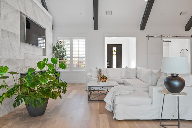 living room with lofted ceiling with beams, visible vents, wood finished floors, and a barn door