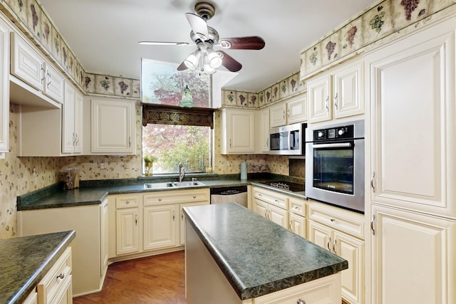 kitchen featuring dark countertops, wallpapered walls, appliances with stainless steel finishes, and a sink