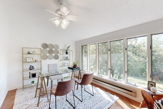 home office featuring light wood-style floors, ceiling fan, a textured ceiling, a baseboard heating unit, and baseboards