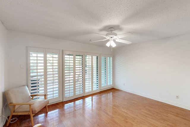 interior space with baseboards, a ceiling fan, wood finished floors, and a textured ceiling