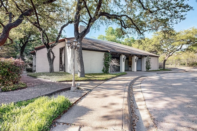 view of front of home featuring a tiled roof, driveway, stucco siding, and fence