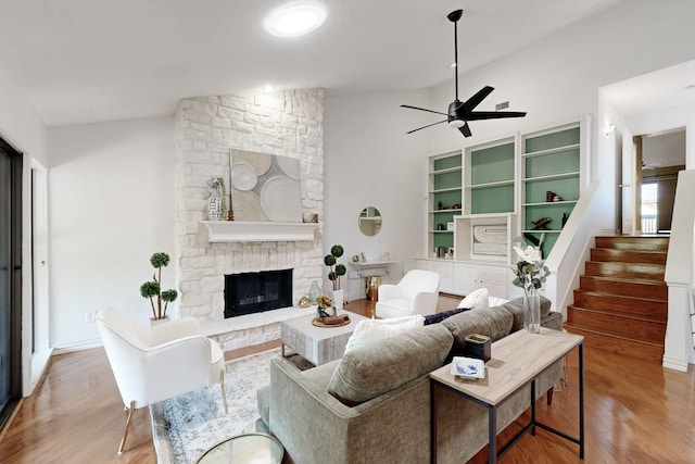 living room with a ceiling fan, vaulted ceiling, wood finished floors, and a fireplace
