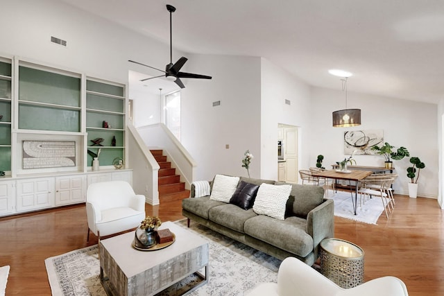 living area with visible vents, ceiling fan, light wood-type flooring, stairway, and high vaulted ceiling