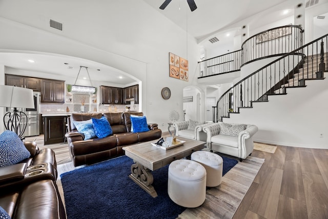 1136 Chickadee Dr, Forney, TX 75126 - living room featuring arched walkways, stairs, a ceiling fan, light wood-type flooring, and a towering ceiling