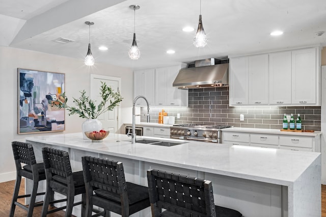 5948 Melshire Dr, Dallas, TX 75230 - kitchen featuring wall chimney range hood, stainless steel stove, wood finished floors, backsplash, and a kitchen island with sink