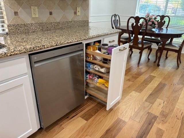 bar featuring backsplash, stainless steel dishwasher, and light wood-style floors