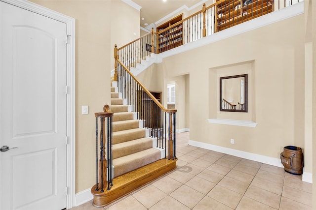 staircase with tile patterned floors, baseboards, a high ceiling, and ornamental molding