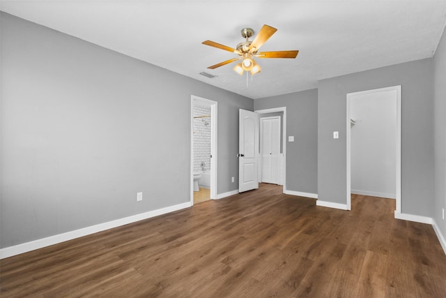 unfurnished bedroom with wood finished floors, visible vents, a walk in closet, a closet, and baseboards