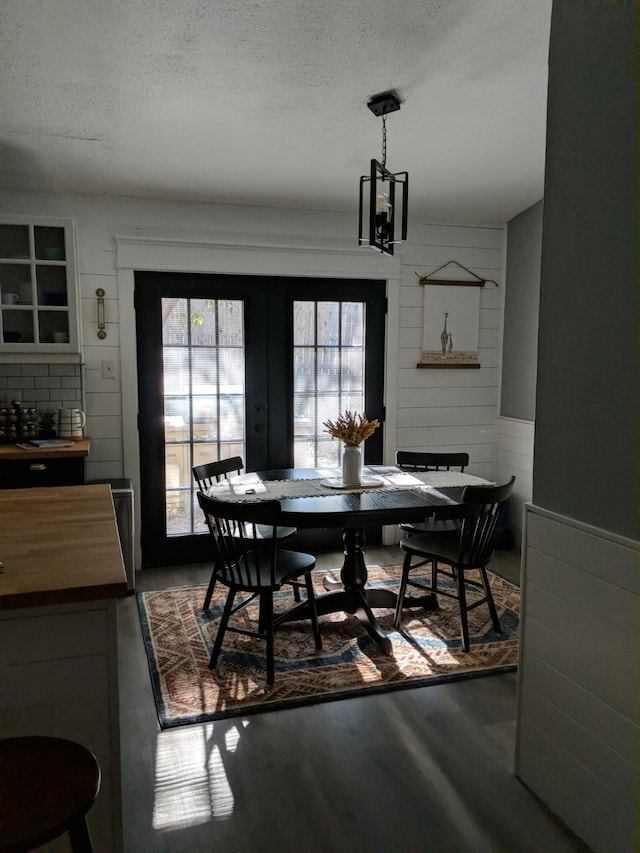 dining space with an inviting chandelier, wooden walls, wood finished floors, french doors, and a textured ceiling