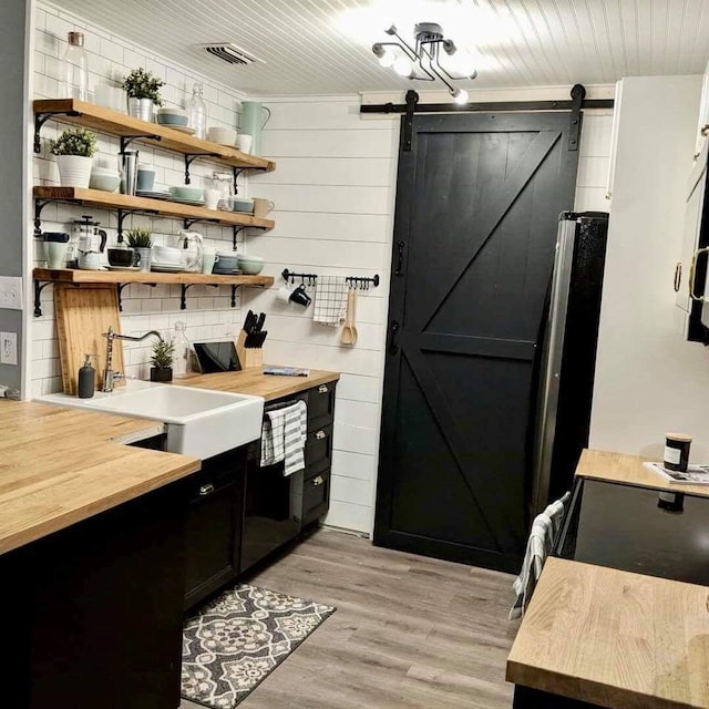 interior space with light wood-style flooring, a sink, a barn door, visible vents, and decorative backsplash
