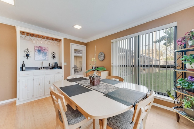 dining room with crown molding, a healthy amount of sunlight, light wood-style floors, and indoor wet bar