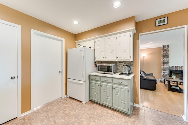 kitchen with freestanding refrigerator, white cabinetry, light tile patterned flooring, light countertops, and stainless steel microwave