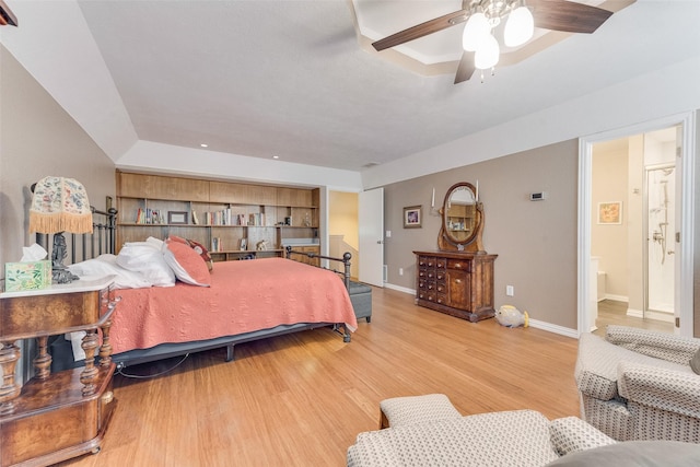 bedroom featuring ensuite bathroom, baseboards, a ceiling fan, a tray ceiling, and light wood finished floors