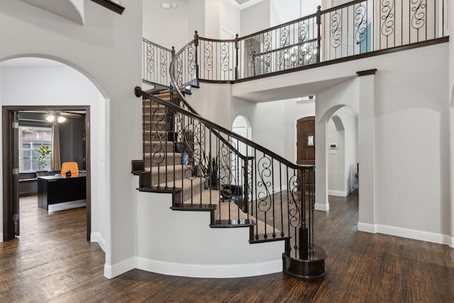 stairs featuring arched walkways, a towering ceiling, baseboards, and wood finished floors