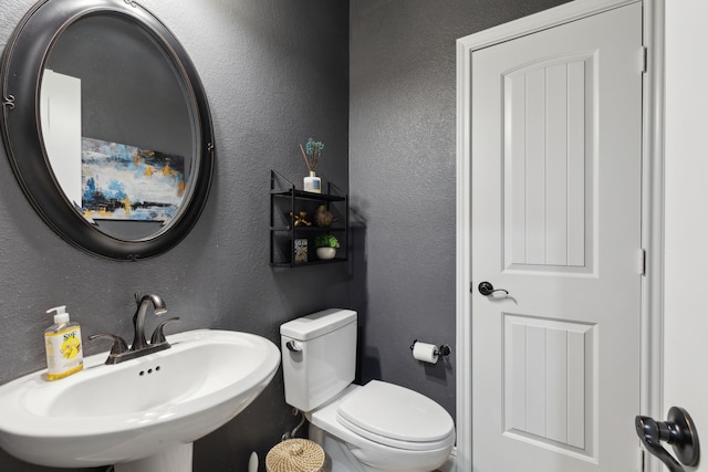 half bathroom featuring toilet, a textured wall, and a sink