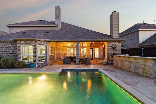 back of property at dusk with an outdoor living space, a chimney, a patio area, and brick siding