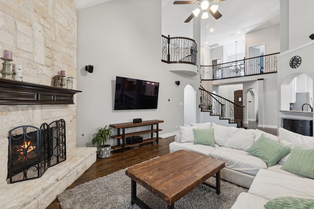 living area featuring arched walkways, a ceiling fan, a fireplace, stairway, and wood finished floors