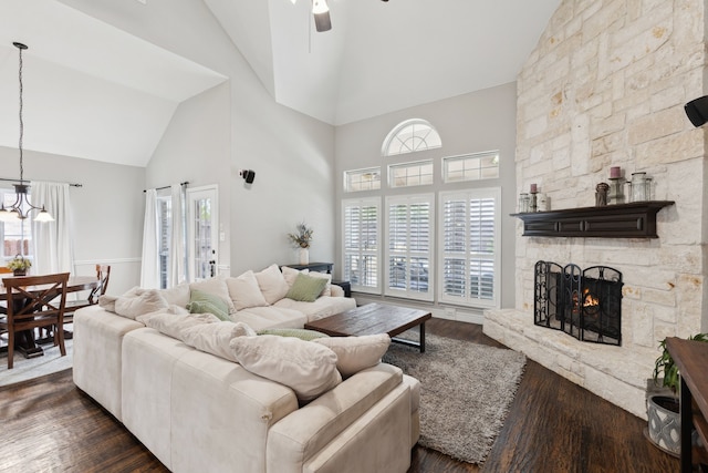 living room with high vaulted ceiling, a fireplace, dark wood-type flooring, and ceiling fan with notable chandelier