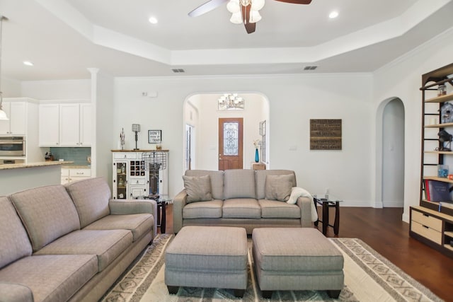 living room with arched walkways, a ceiling fan, dark wood-type flooring, and a raised ceiling