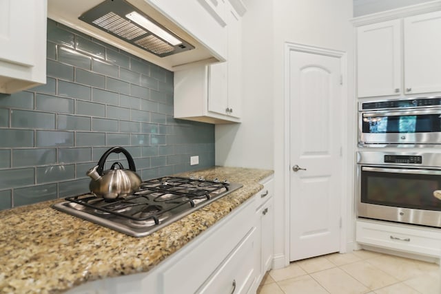 kitchen featuring white cabinets, stainless steel appliances, tasteful backsplash, custom exhaust hood, and light tile patterned floors