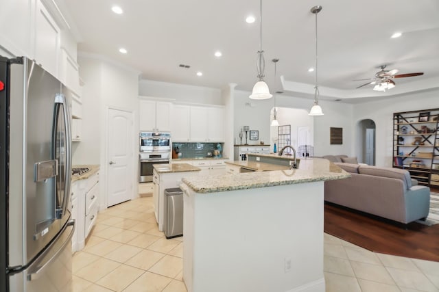 kitchen with arched walkways, a spacious island, light tile patterned flooring, open floor plan, and appliances with stainless steel finishes