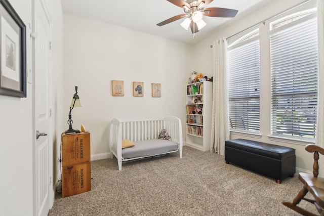carpeted bedroom with a nursery area, a ceiling fan, and baseboards