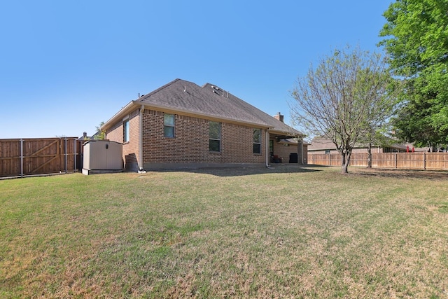 back of house featuring a lawn, a fenced backyard, a storage unit, and brick siding