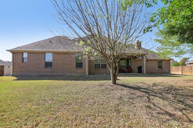 back of house with brick siding, fence, and a lawn