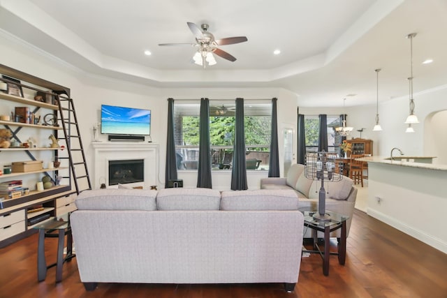 living area featuring dark wood-style flooring, baseboards, a ceiling fan, a fireplace, and a raised ceiling