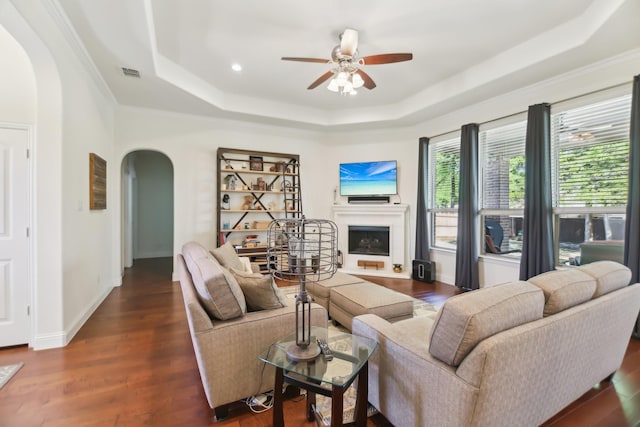 living area featuring ceiling fan, arched walkways, a tray ceiling, a fireplace, and visible vents