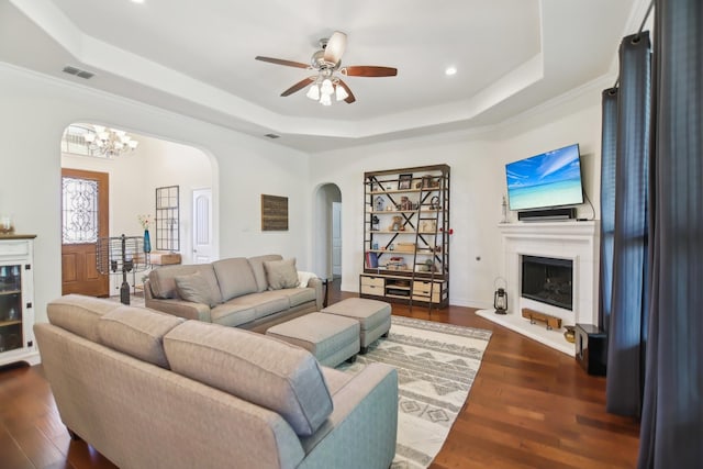 living room featuring a raised ceiling, visible vents, arched walkways, dark wood-style flooring, and ceiling fan with notable chandelier