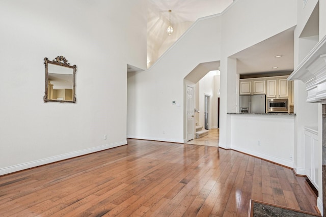 604 Nelson Ct, Plano, TX 75025 - unfurnished living room with arched walkways, baseboards, a high ceiling, and light wood-style floors