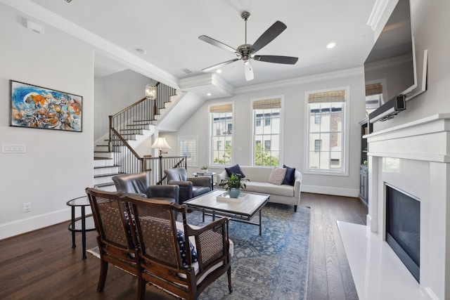 living area with a ceiling fan, dark wood finished floors, baseboards, a glass covered fireplace, and ornamental molding