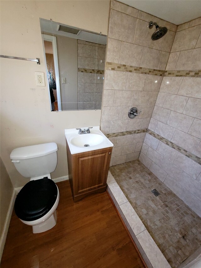 full bathroom with toilet, a tile shower, vanity, and wood finished floors