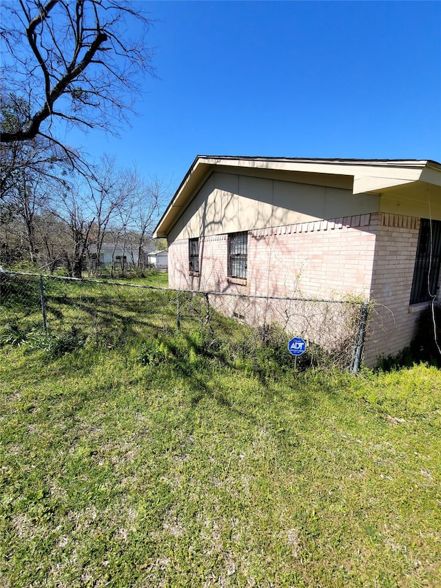 view of side of property with a yard, fence, and brick siding
