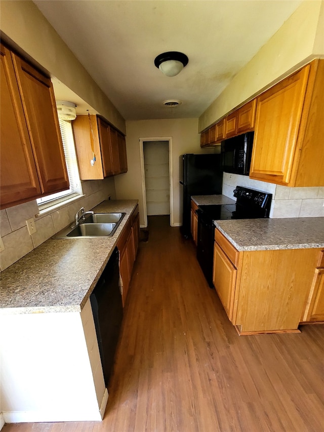 kitchen featuring a sink, backsplash, black appliances, and wood finished floors