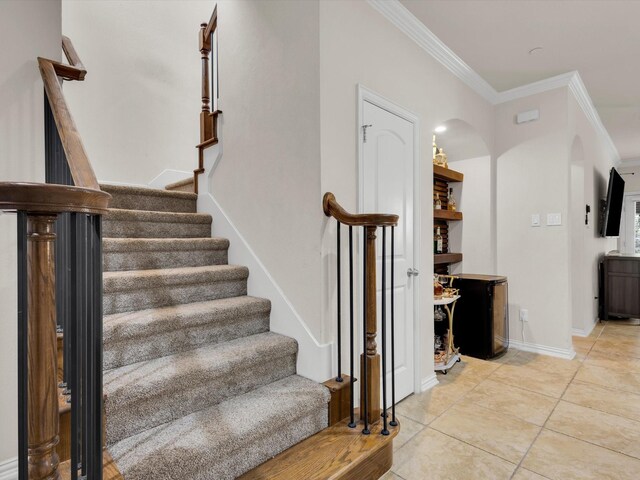 stairway featuring arched walkways, baseboards, crown molding, and tile patterned flooring