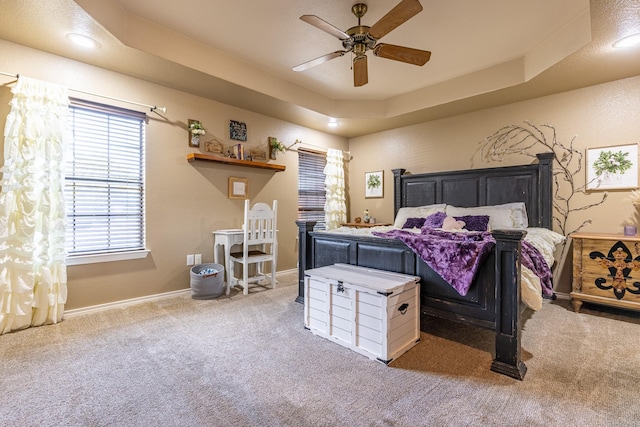 carpeted bedroom with a ceiling fan, a raised ceiling, and baseboards