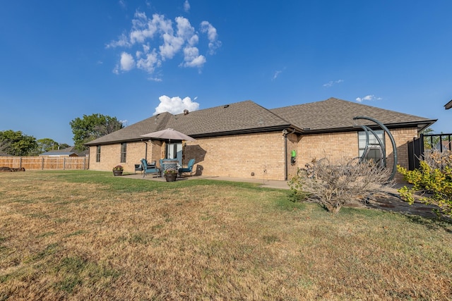 back of property featuring a shingled roof, a patio area, a yard, brick siding, and fence