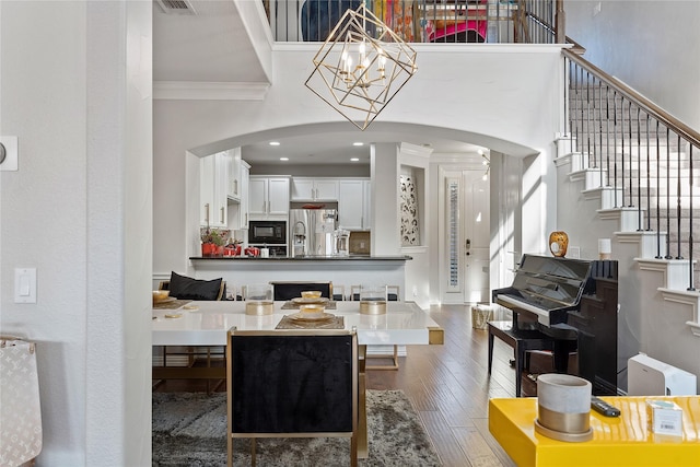 living area featuring a towering ceiling, ornamental molding, stairs, arched walkways, and wood finished floors