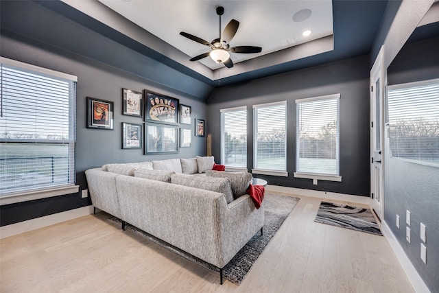 living area with a raised ceiling, wood finished floors, ceiling fan, and baseboards